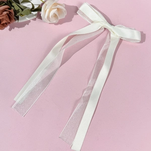 Close-up of cream white ballet style tulle ribbon bow hair clip on soft pink background