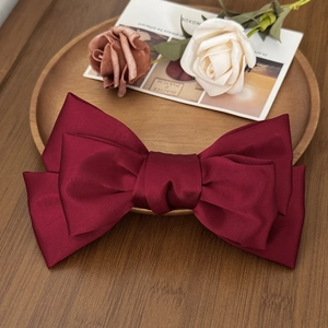 Close-up of a large burgundy satin bow hair clip placed on a rustic wooden tray