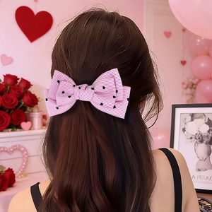 Barrette nœud rayée rose et blanc avec motif cœur sur cheveux bruns ondulés
