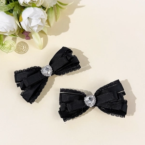 Détail de barrettes à nœud en dentelle noire avec cristal cœur sur fond beige