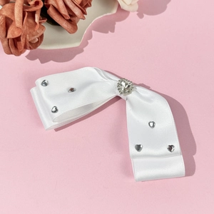 Close-up of white satin bow hair clip featuring a sparkling rhinestone heart center