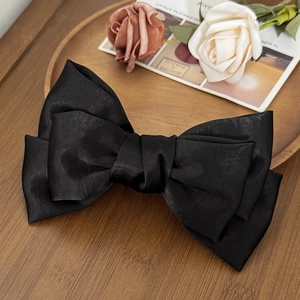 Macro detail of a large black satin bow hair clip placed on a wooden tray with roses