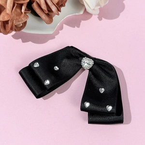 Detail of black satin bow hair clip with sparkling rhinestone hearts on pink background