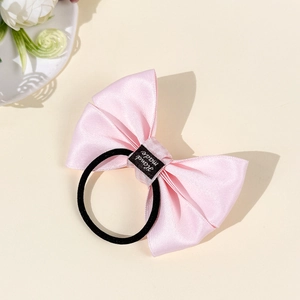 Detailed shot of pink satin plaid bow hair tie with Hand Made label and black elastic