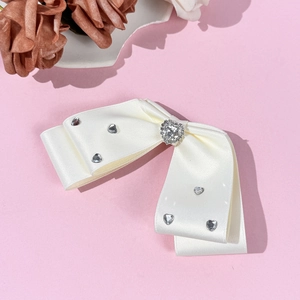 Elegant white satin bow hair clip with heart-shaped rhinestones on pink background