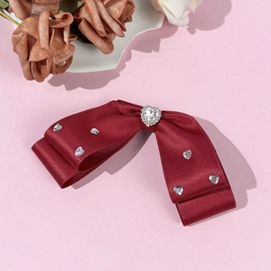 Detail of burgundy satin double bow hair clip with sparkling heart-shaped rhinestones