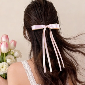 Dettaglio del fermaglio per capelli a fiocco in raso rosa con bordi dorati e nastri
