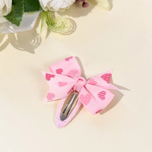 Detailed view of a pink grosgrain bow hair clip with heart patterns on a metal snap clip