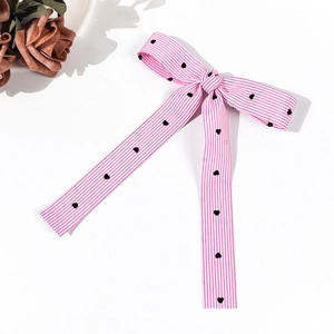 Detail of pink and white striped bow hair clip with embroidered black hearts and long ribbons