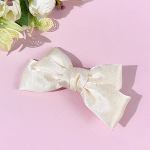 Close-up of elegant cream satin double-layered bow hair clip with glossy silk texture