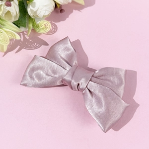 Detailed view of a pink satin bow hair clip featuring a smooth, silky texture and elegant finish