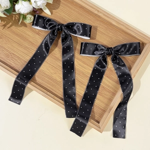 Gros plan de barrettes à pois en satin noir avec longs pompons sur un plateau en bois