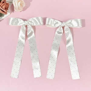 Gros plan de barrettes à nœuds en satin blanc à pois noirs avec de longs rubans fluides