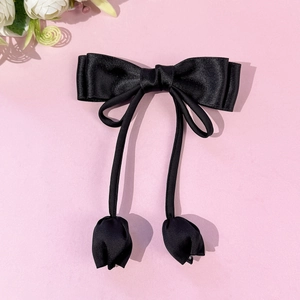 Détail d'un nœud papillon en satin noir élégant avec des tulipes pendantes sur fond rose