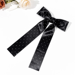 Detail view of a black polka dot satin bow hair clip with elegant long streamers