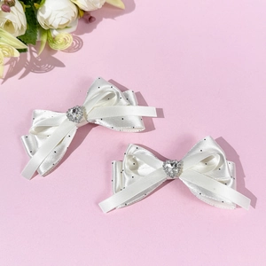Detail view of white silk bow hair clips with black polka dots and silver heart rhinestones