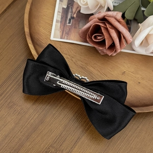 Classic black satin bow hair clip with silver metal alligator clip on a wooden tray