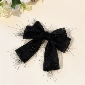 Détail de la pince à cheveux noire avec franges pailletées et nœud sur fond beige