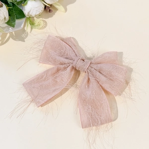 Gros plan sur la barrette nœud rose poudré avec textures frangées et nœud en tissu chic