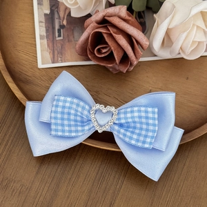 Detail of blue plaid bow hair clip with heart rhinestone on elegant wooden tray