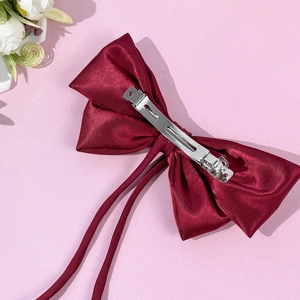 Elegant wine red satin bow hair clip with long streamers on soft pink background