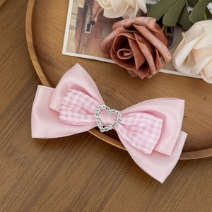 Pink satin bow hair clip with plaid ribbon and heart-shaped rhinestone center on wood