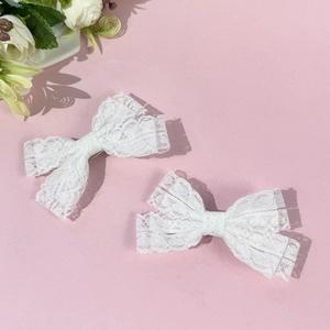 Détail de barrettes nœuds en dentelle blanche lot de 2 sur un fond rose doux