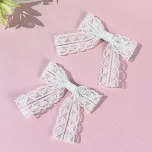 Lot de deux barrettes à nœuds en dentelle blanche avec motifs de cœurs sur fond rose