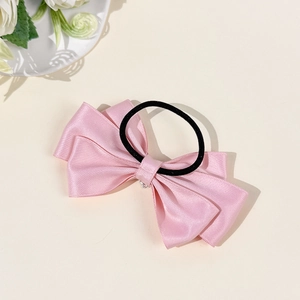 Detail view of a pink satin bow hair tie with rhinestone heart on a beige background