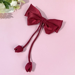 Close-up of wine red satin bow hair clip with elegant long ribbons and tulip floral details