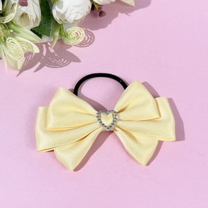 Detail of light yellow satin bow hair tie with rhinestone heart and black elastic band