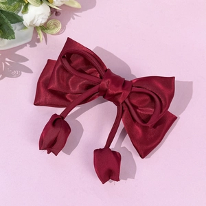 Elegant deep red satin bow hair clip with hanging tulip charms on light pink surface
