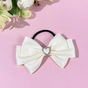 Close-up of white satin bow hair tie with sparkling rhinestone heart on pink background
