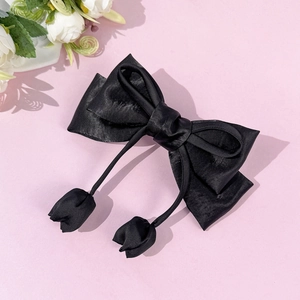 Detail of elegant black satin bow hair clip featuring tulip pendant tassels on pink background