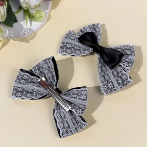 Détail de deux pinces à cheveux Lolita en dentelle blanche avec nœud noir et métal argenté