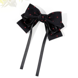 Close-up of black satin bow hair clip with red polka dots and long hanging ribbons