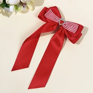 Détail de la barrette à nœud en satin rouge avec motif à carreaux et strass en cœur
