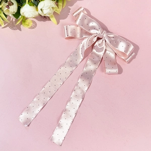 Gros plan d'une pince à cheveux à nœud rose à pois avec de longs rubans élégants