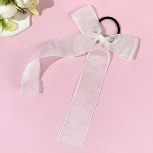 Detailed view of white organza ribbon bow hair tie on a soft pink background