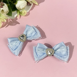 Detail view of two light blue lace bow hair clips with heart crystal centers on pink surface