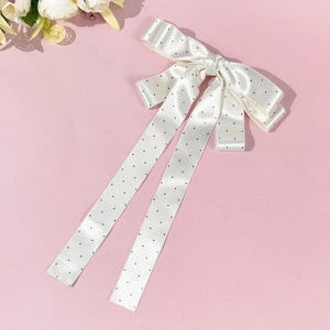 Détail du nœud papillon en satin blanc à pois noirs sur fond rose pour cheveux élégants