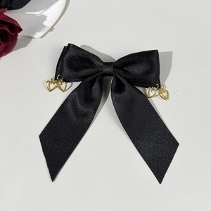 Detail of black satin bow hair clip with golden heart-shaped pendants on gray background