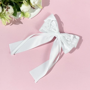 Détail du nœud en satin blanc avec bordure en dentelle et longs rubans sur fond rose