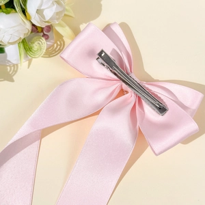 Pince à cheveux nœud en satin rose avec clip en métal argenté sur fond esthétique