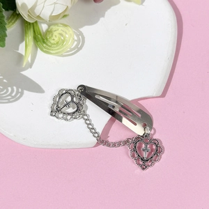 Pince à cheveux cœur en métal argenté avec pendentif croix sur fond rose