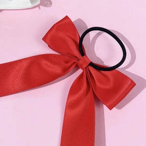 Gros plan d'un chouchou noeud en ruban rouge avec texture satinée sur fond rose clair