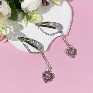 Détail de pinces à cheveux coeur argenté avec chaînes et croix sur un fond rose doux