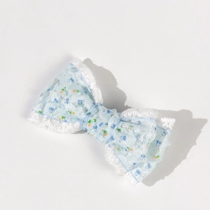 Dettaglio del fermaglio per capelli a fiocco in pizzo floreale con fiori blu e bordi bianchi