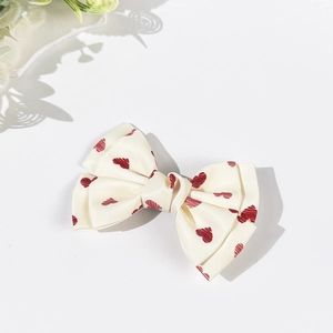 Detailed view of cream bow hair clip with red heart patterns on ribbed satin fabric