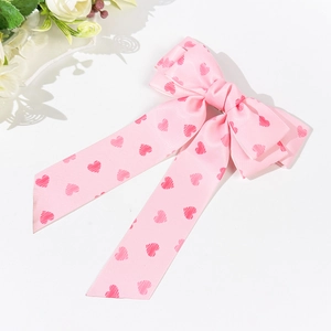Close-up of pink satin bow hair clip featuring red heart patterns and long ribbons